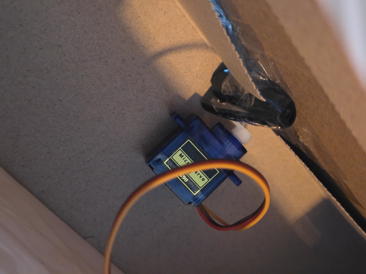Close-up of SG90 servo latch mechanism inside cardboard box